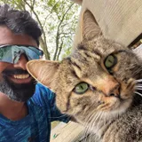 Shreyans in sports sunglasses, grinning next to a tabby cat that has pushed its face right up to the camera.